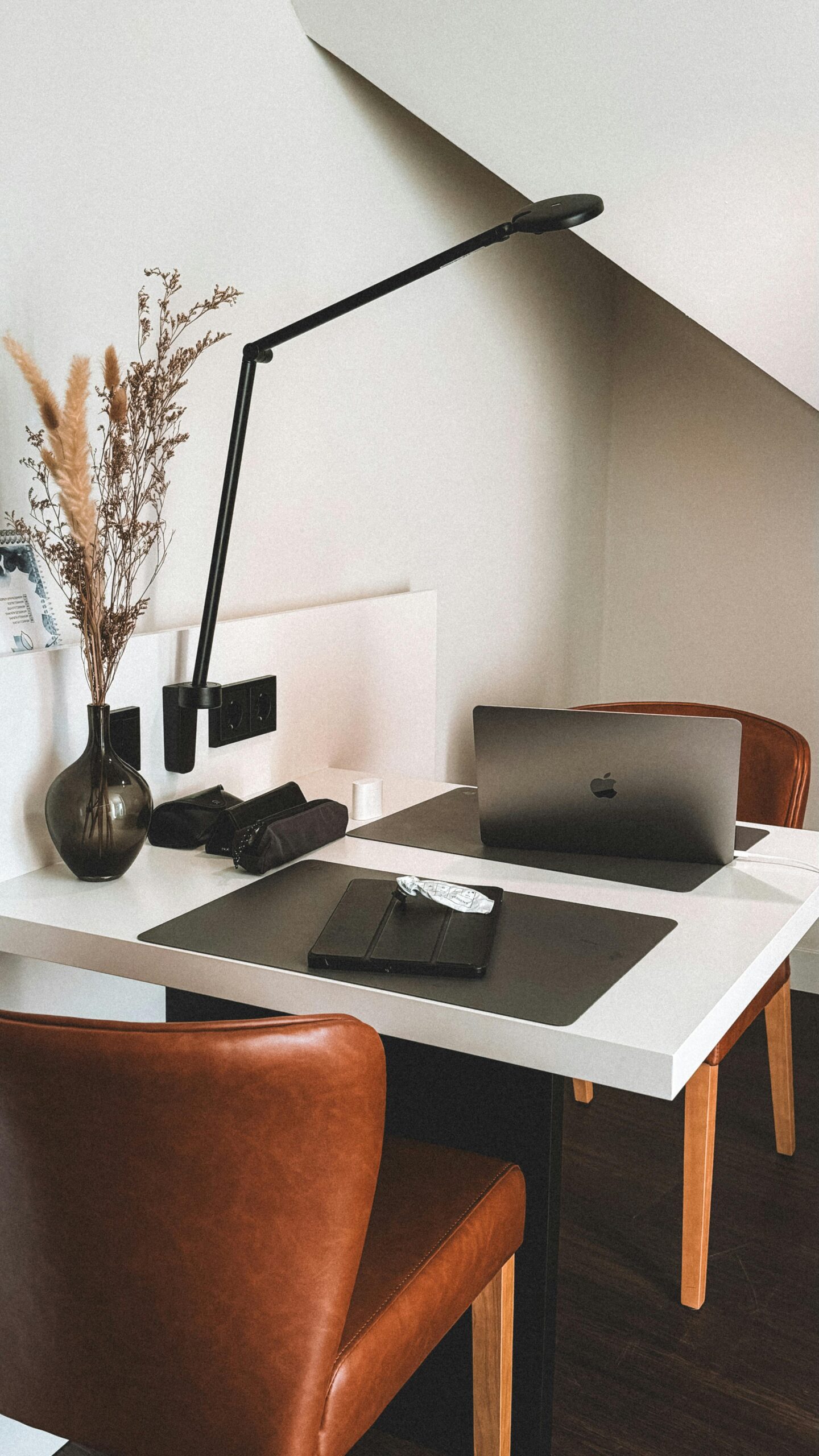 Sleek home office interior with a laptop and modern lamp on a white desk.